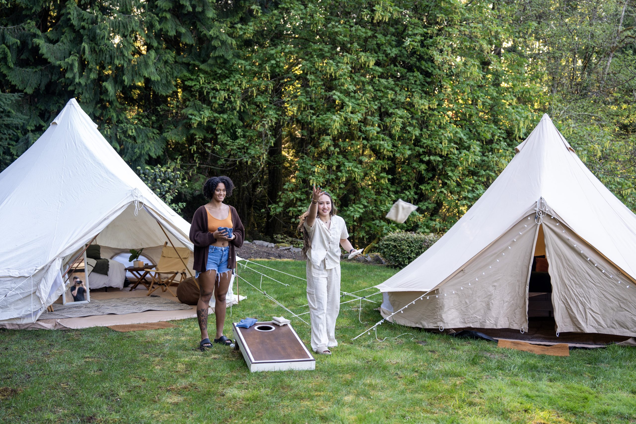 two women playing cornhole in front of glamping tents